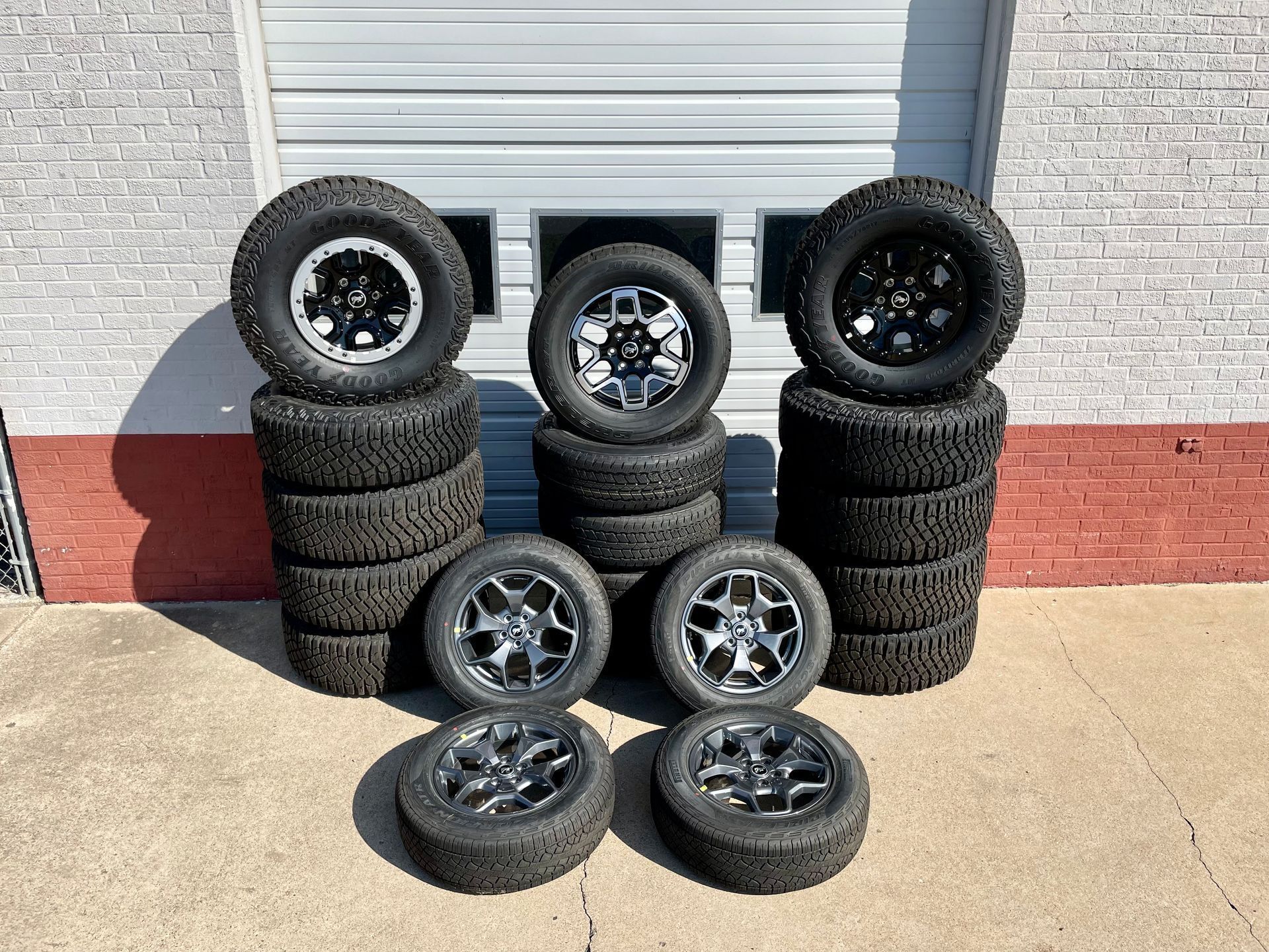 A bunch of tires and wheels are stacked on top of each other in front of a garage door.