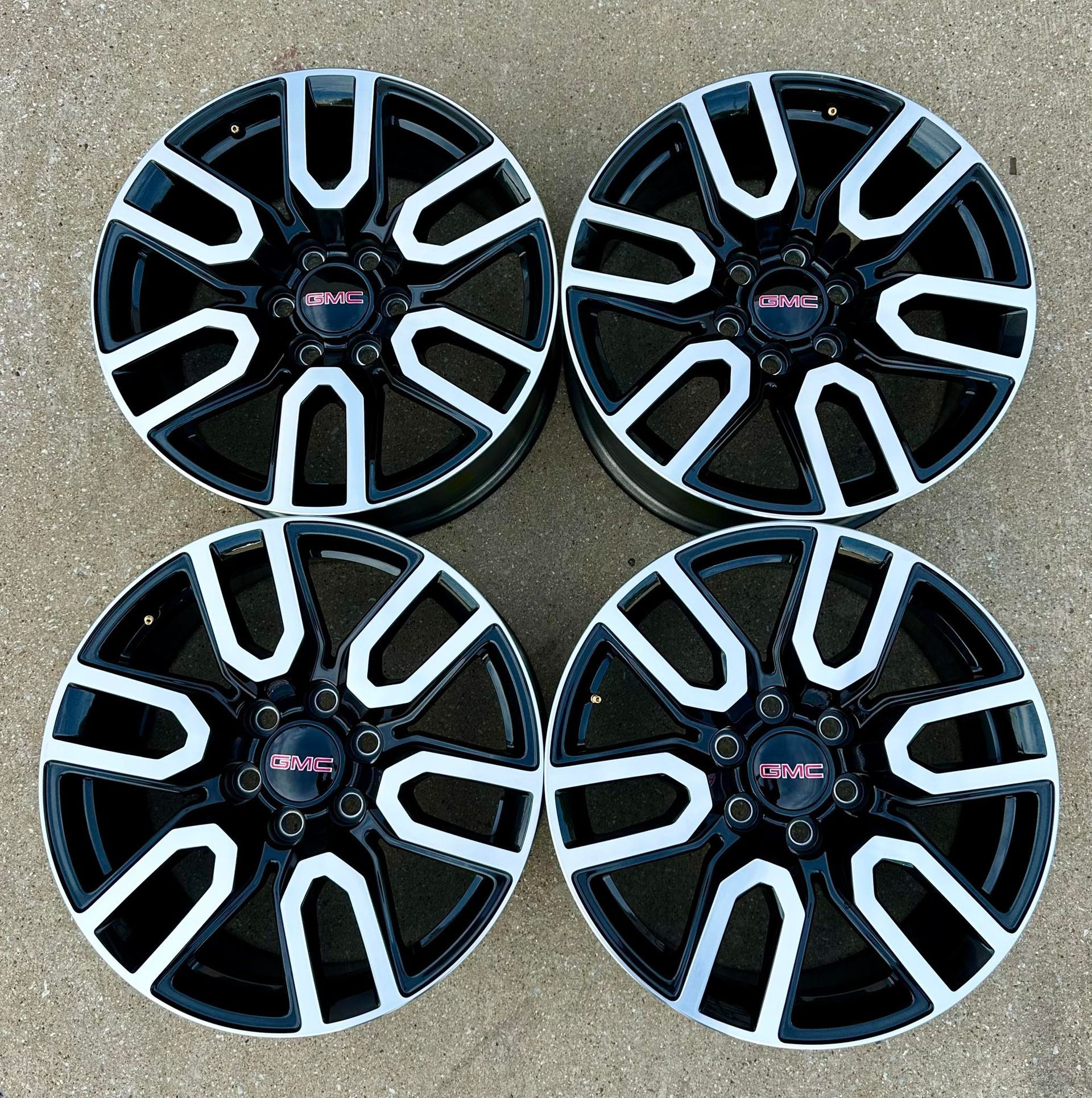 Four black and white gmc wheels are sitting on a concrete surface.