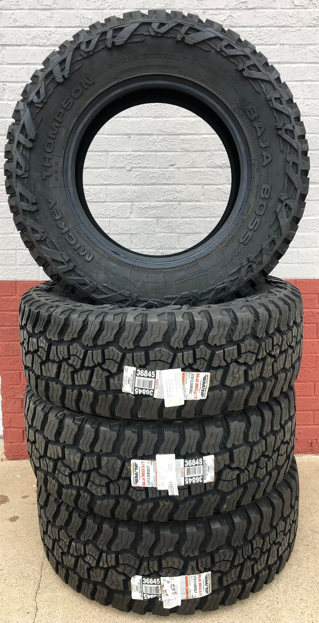 Four tires are stacked on top of each other in front of a brick wall.