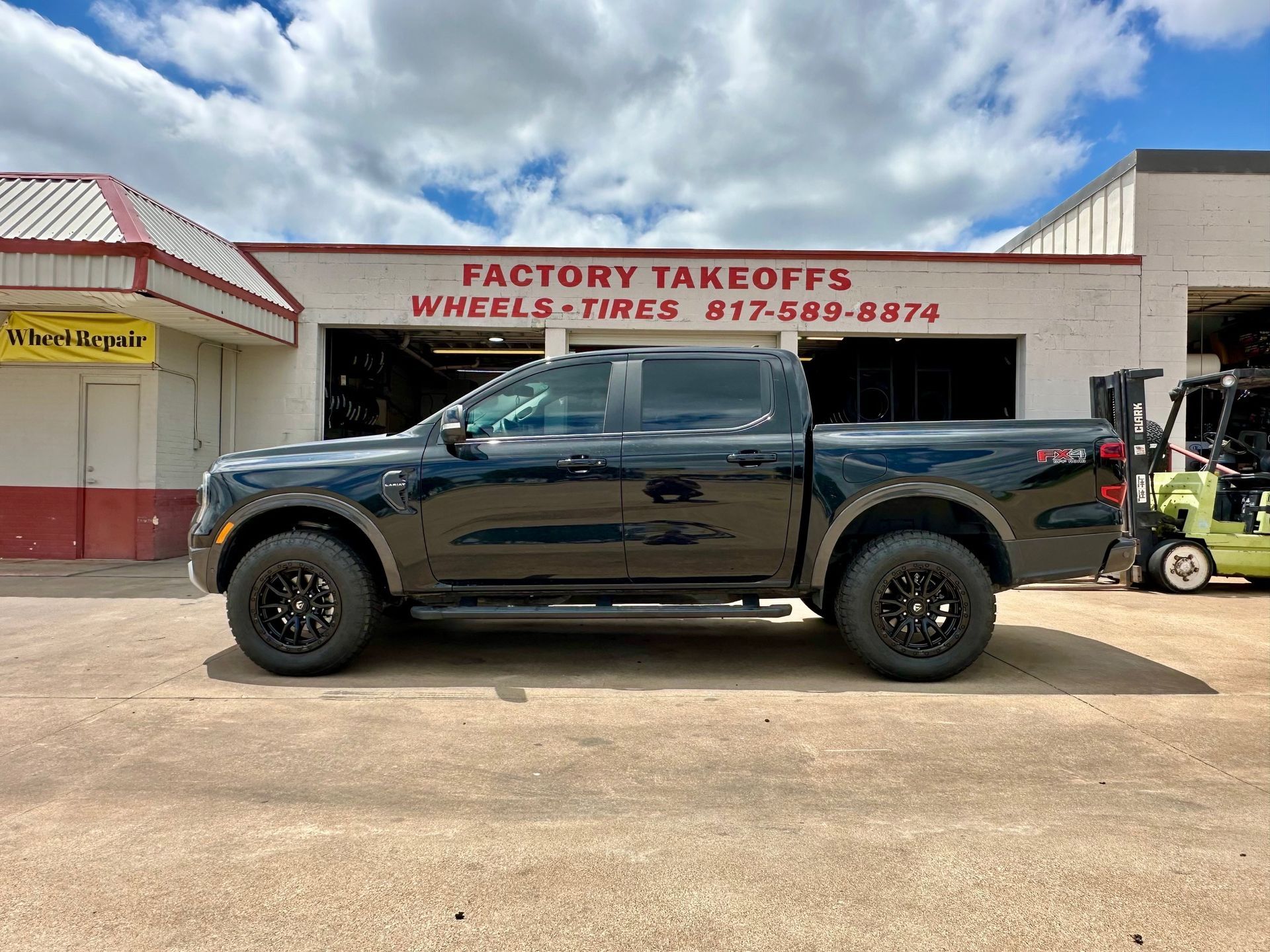A black truck is parked in front of a factory takeoffs wheels and tires store.