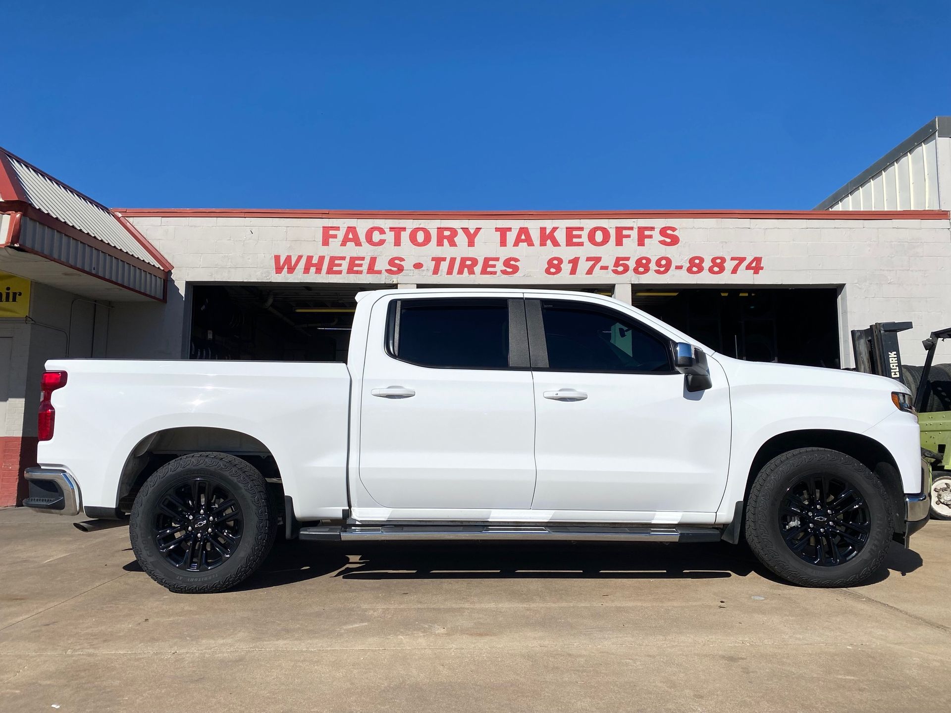 A white truck is parked in front of a building that says factory takeoffs wheels tires.