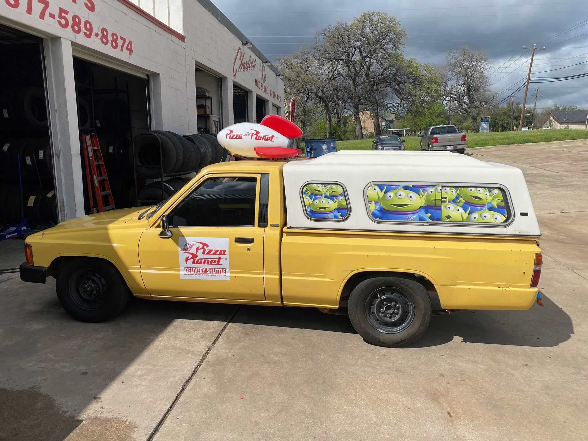 A yellow toy story truck is parked in front of a garage.
