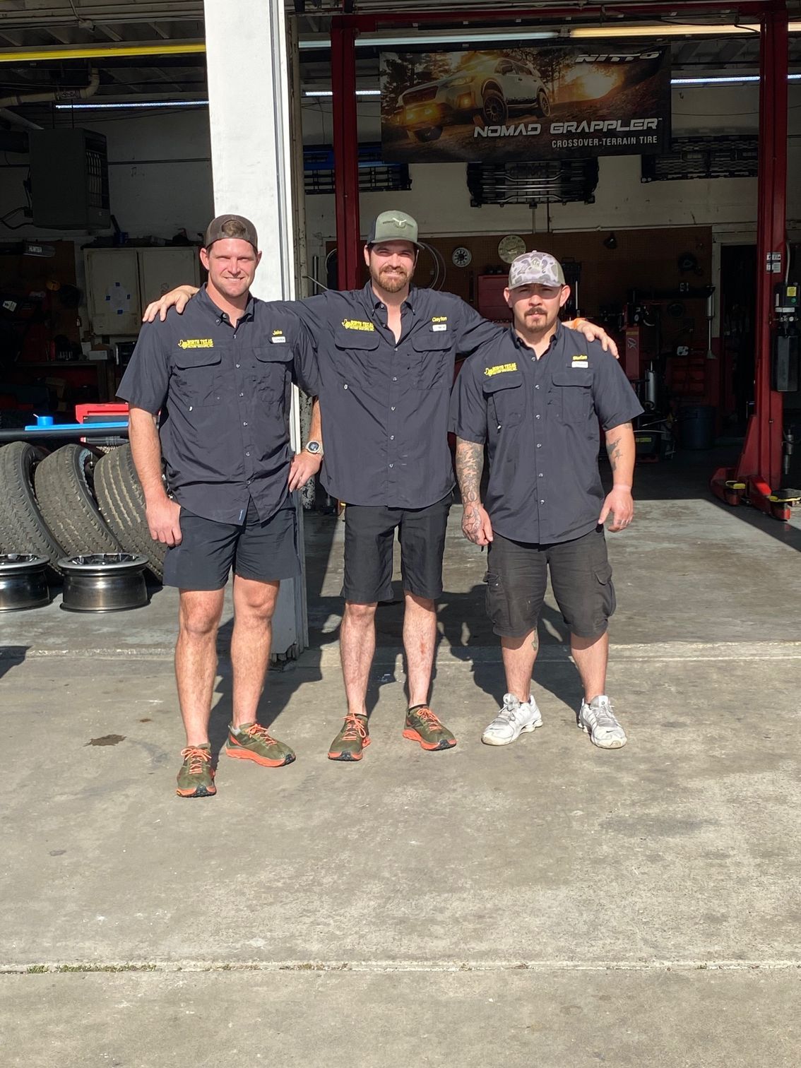 Three men are posing for a picture in front of a tire shop.