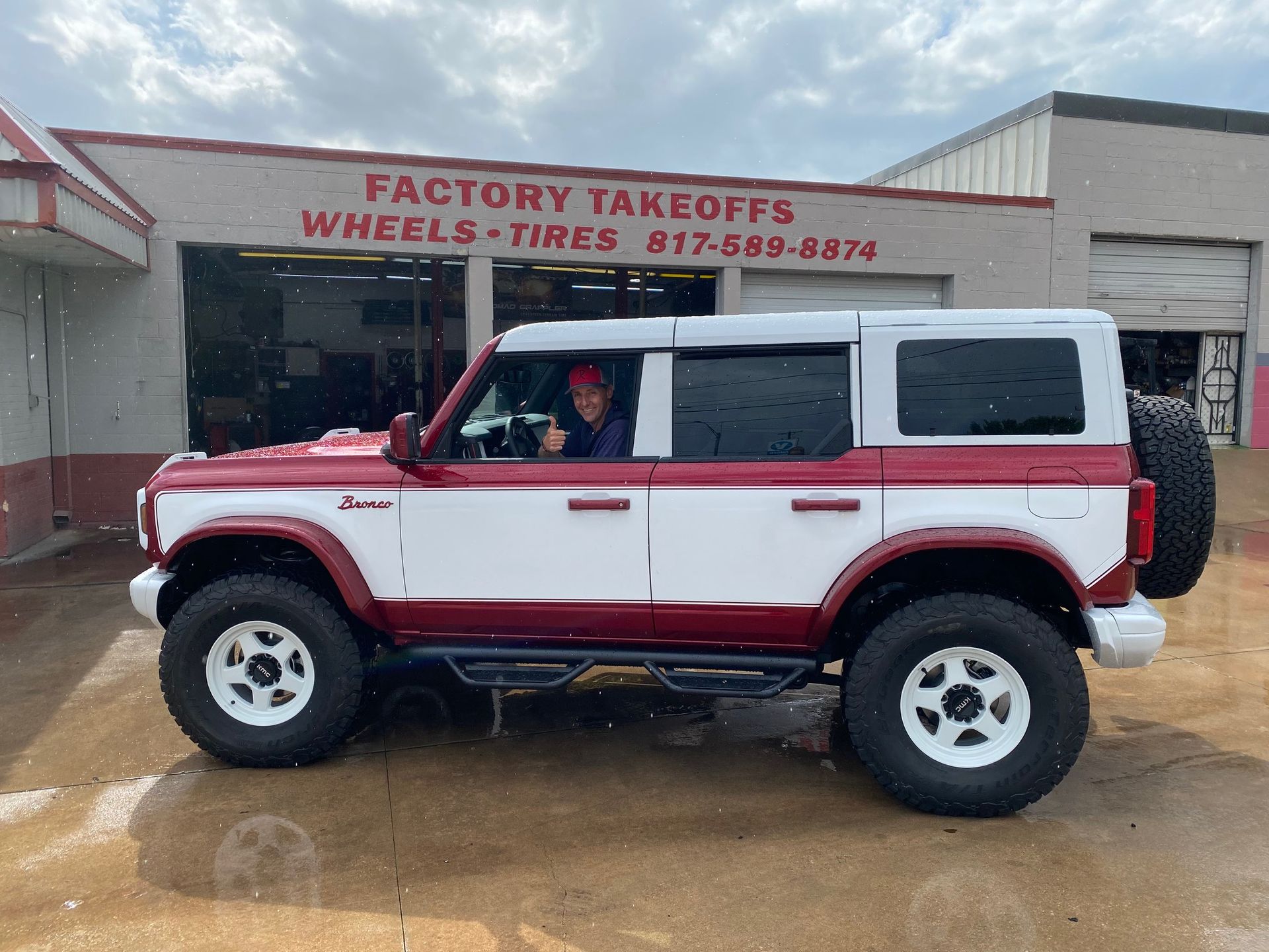 A red and white jeep is parked in front of a factory takeoffs wheels and tires store.
