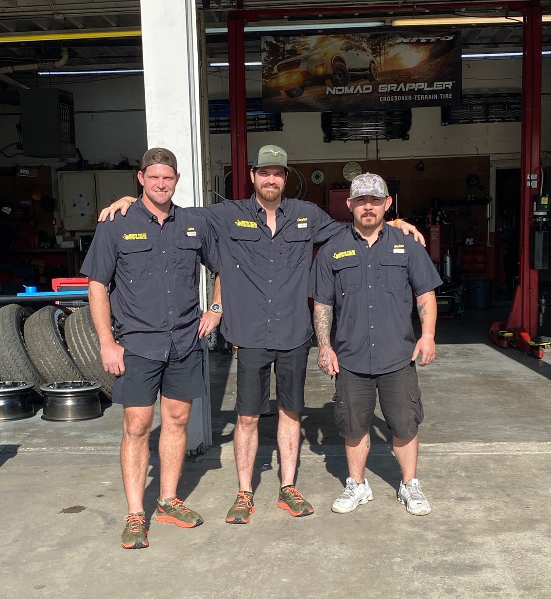 Three men are posing for a picture in front of a garage