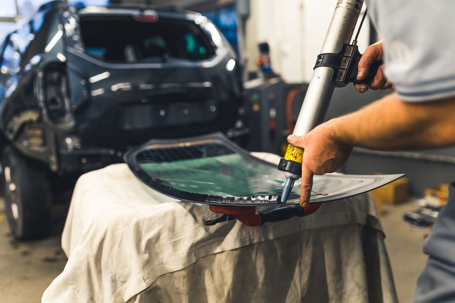 A person applying sealant to a car window. A black SUV is in the background. The person is in a workshop.