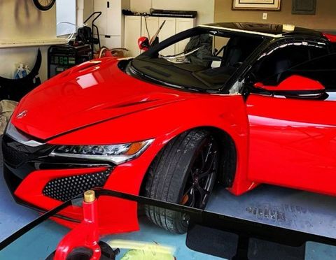 Bright red Honda NSX sports car with a black roof and open door, parked in a garage.