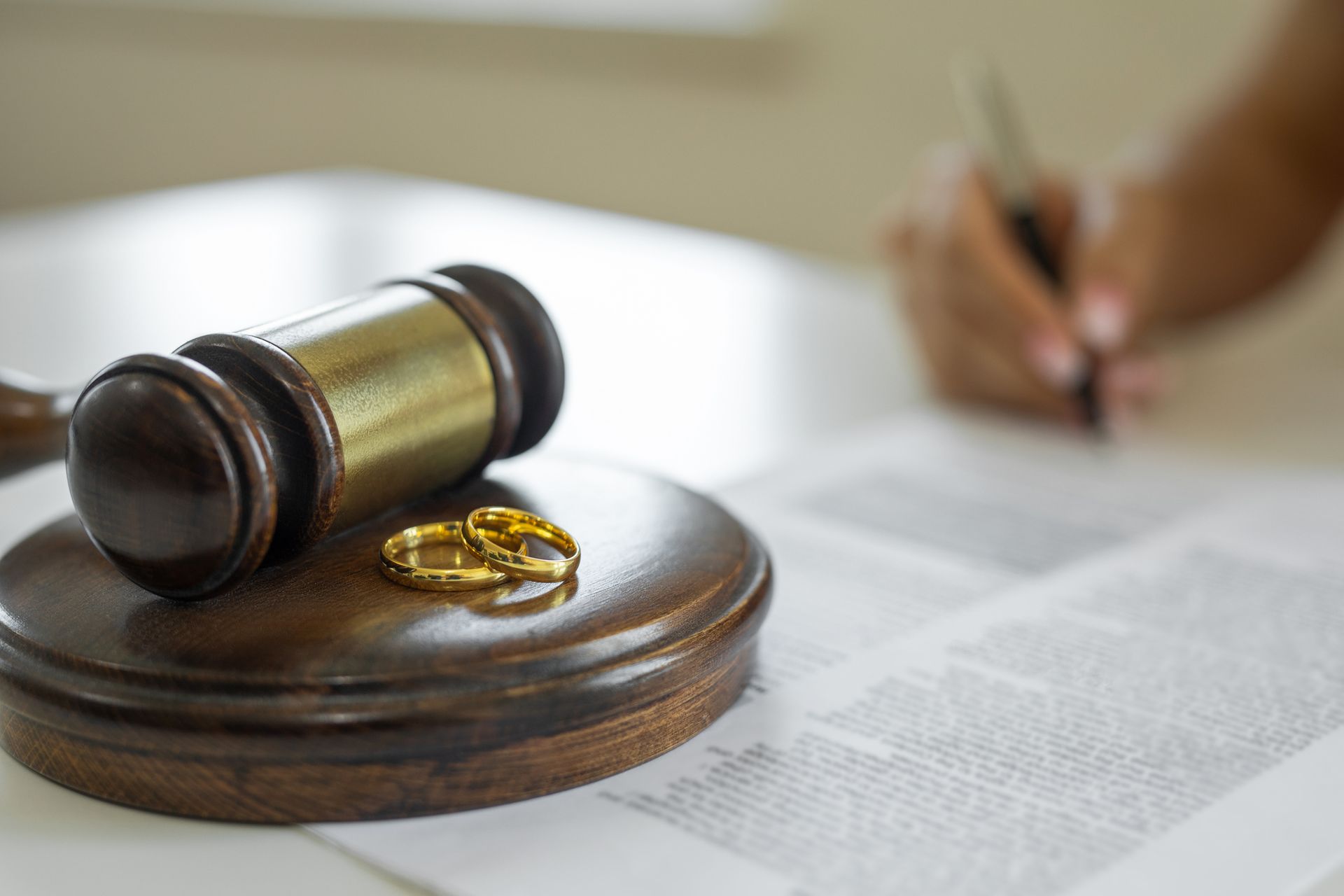 A gavel and wedding rings on it, and a person signing a contract in a divorce lawyer's office.