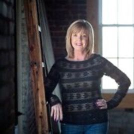 A woman in a black sweater is standing in front of a window.