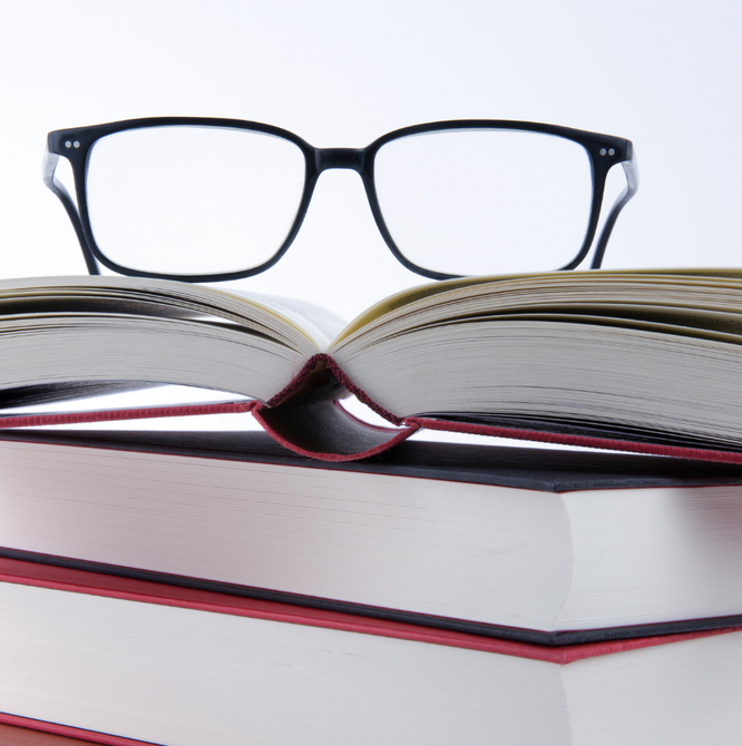 A pair of glasses sits on top of a stack of books