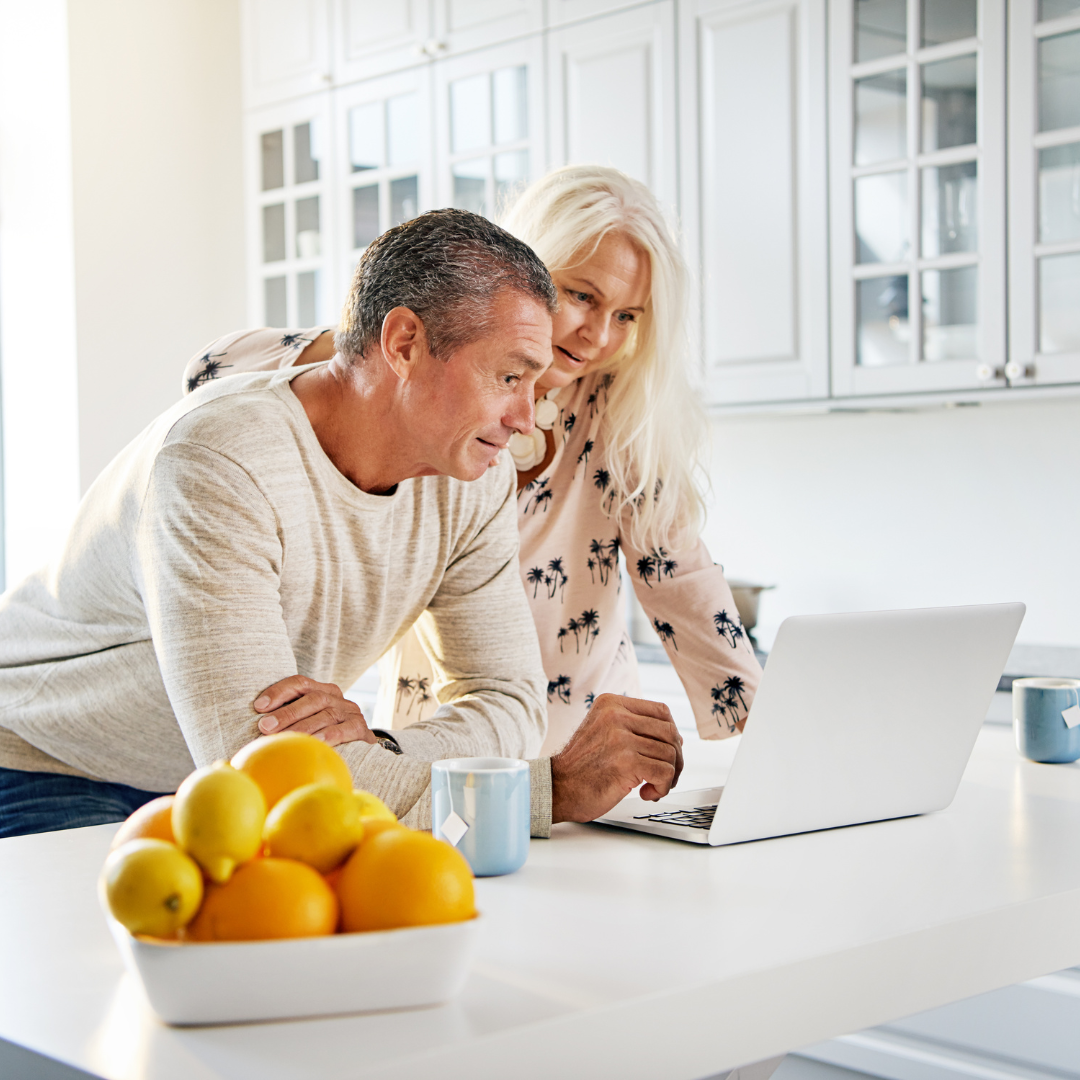 A man and a woman are looking at a laptop in a kitchen.