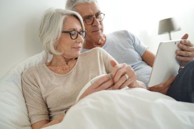 Senior married couple relaxing in bed looking at tablet