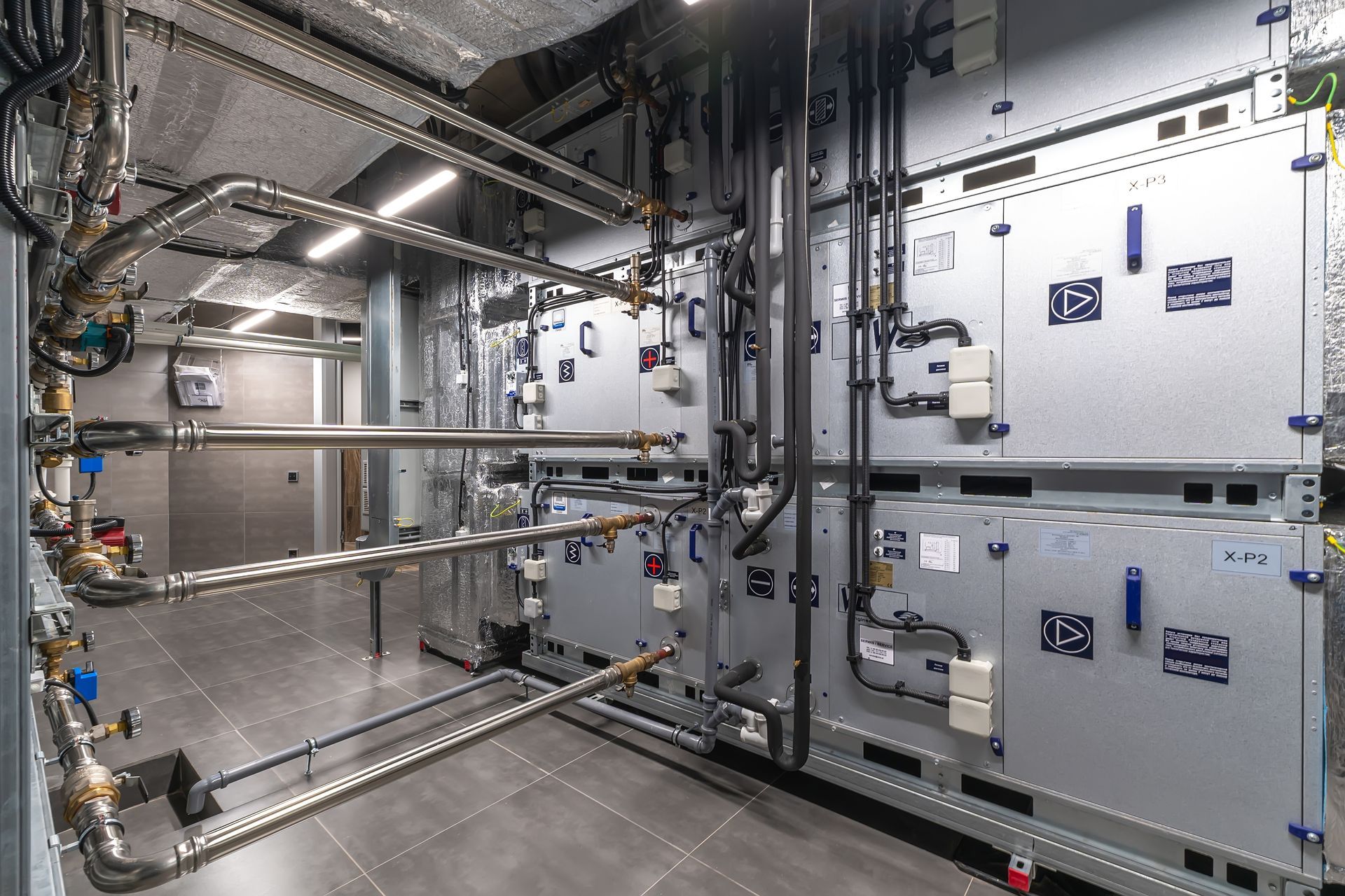 Silver ventilation ducts and pipes installed on a white ceiling near a window.