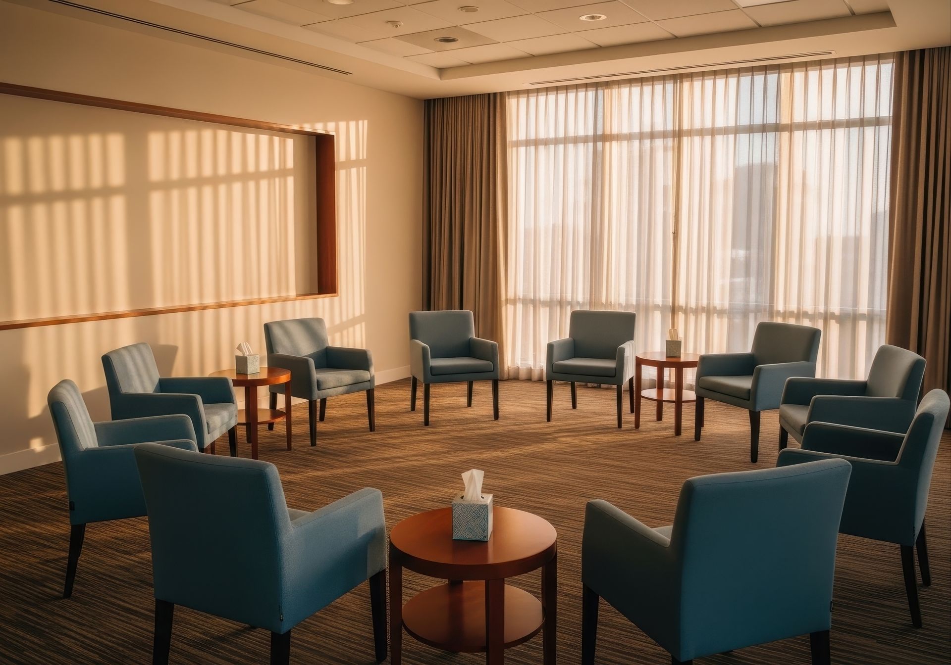 A room with blue chairs arranged in a circle for group therapy, lit by sunlight.