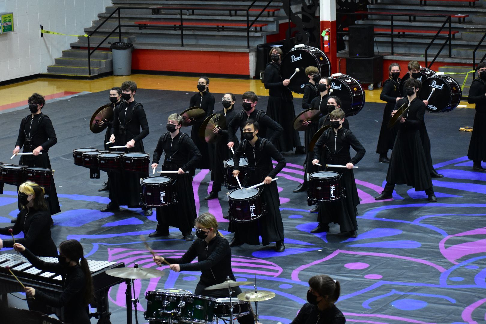 A marching band is playing drums on a stage in a gym.