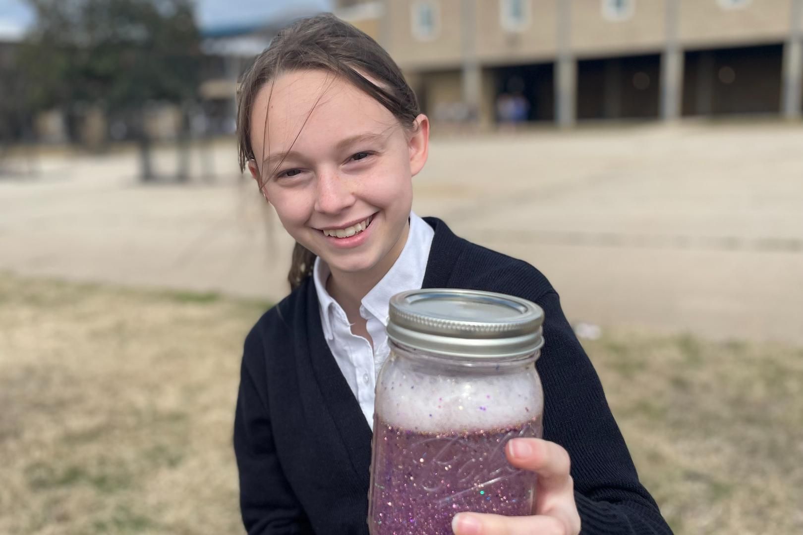 A young girl is holding a jar of purple liquid.