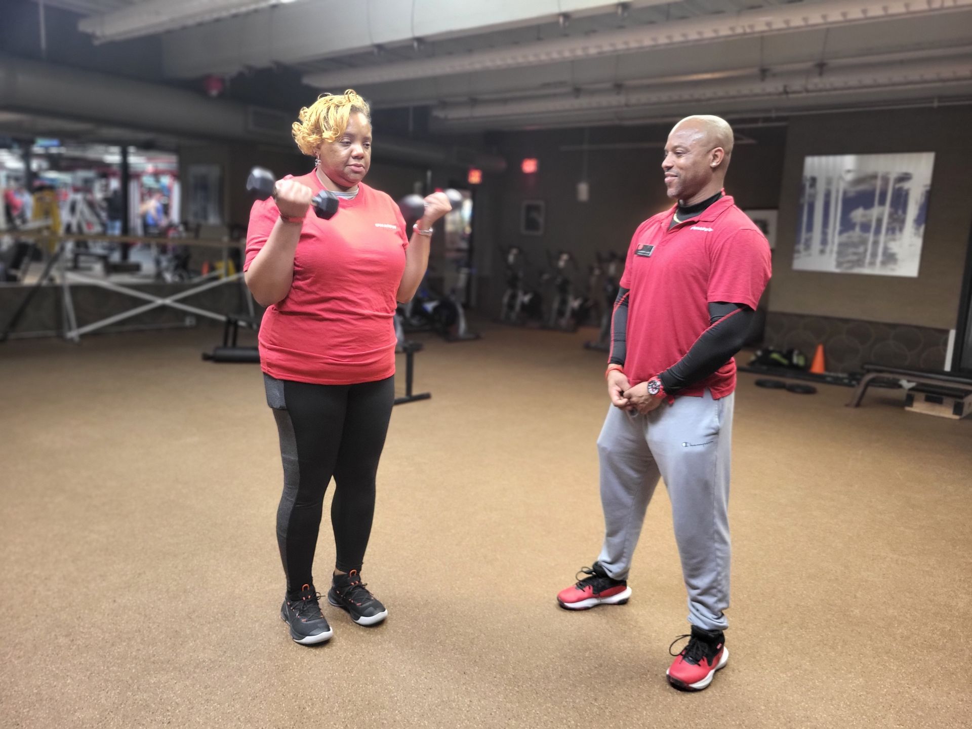 Woman lifting dumbbells at gym, personal trainer watches.