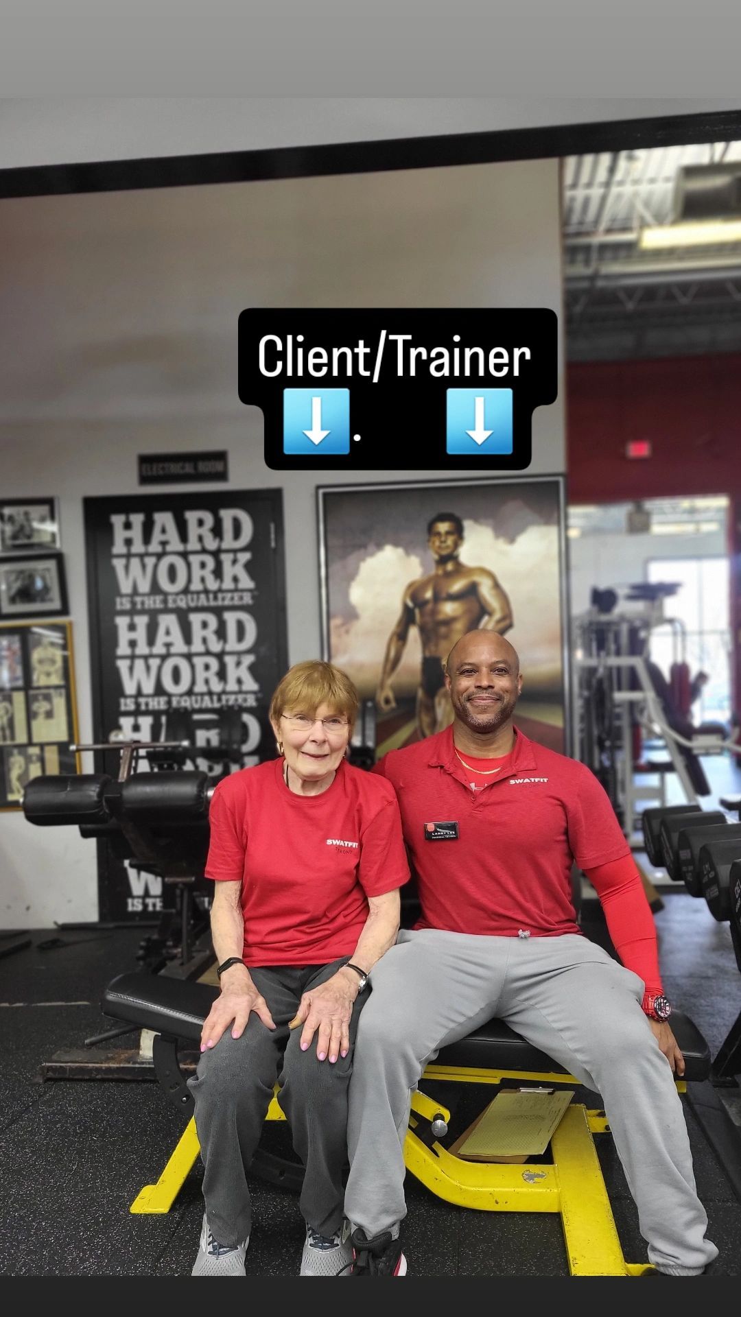 Client and trainer seated on weight bench. Both wear red shirts, smiling, in a gym. 