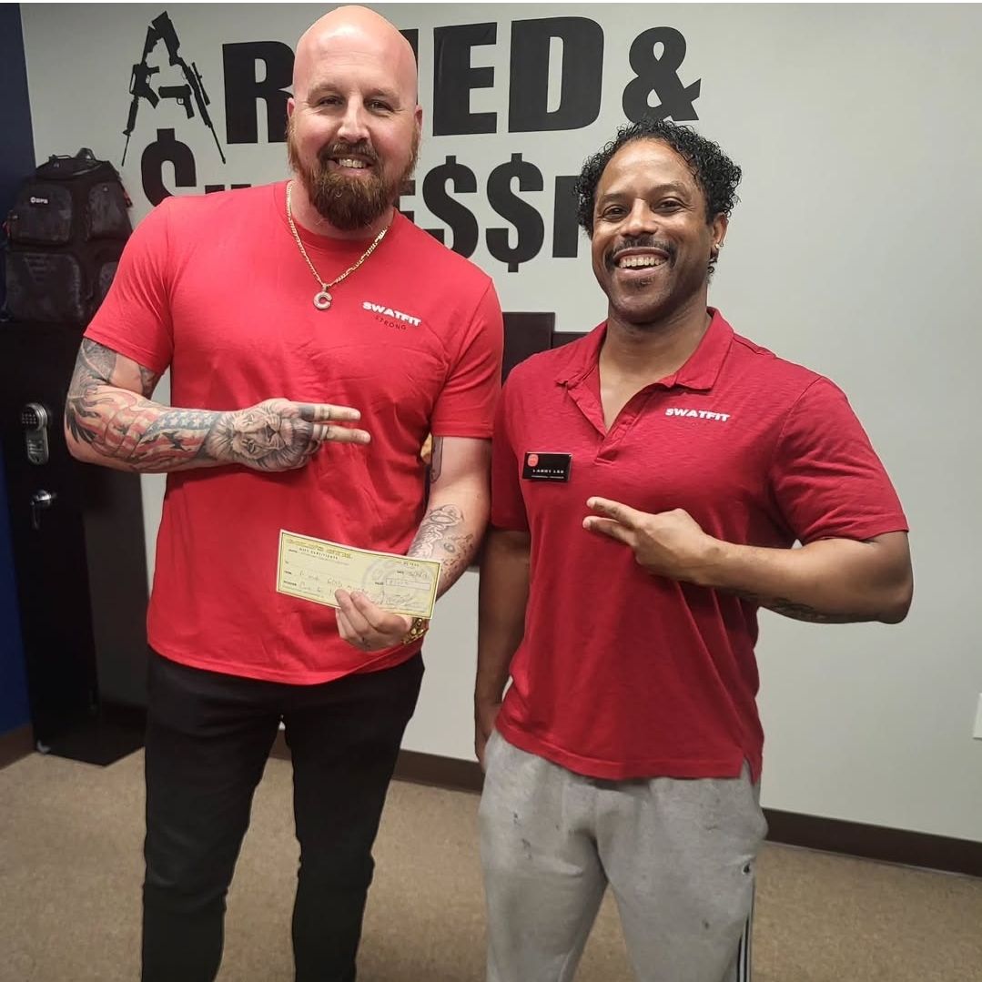 Two men in red shirts holding cash, making peace signs, smiling in a room with