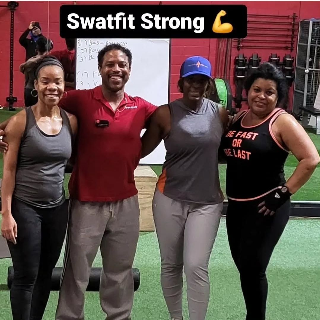 Four people pose together in a gym. A person in red shirt is in the middle with the other three people flanking him. 