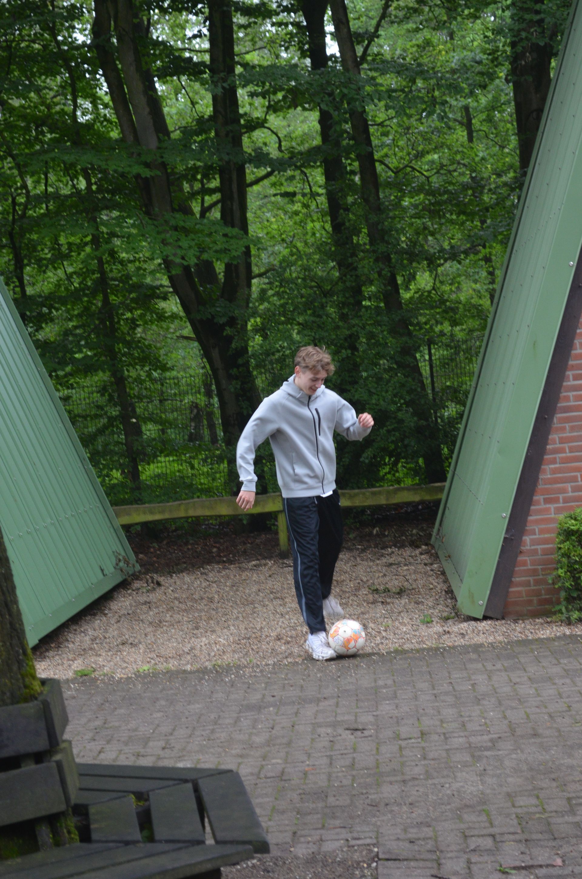 Ein kleiner Junge kickt auf einem gepflasterten Gehweg einen Fußball - Karate-Jugendfreizeit.