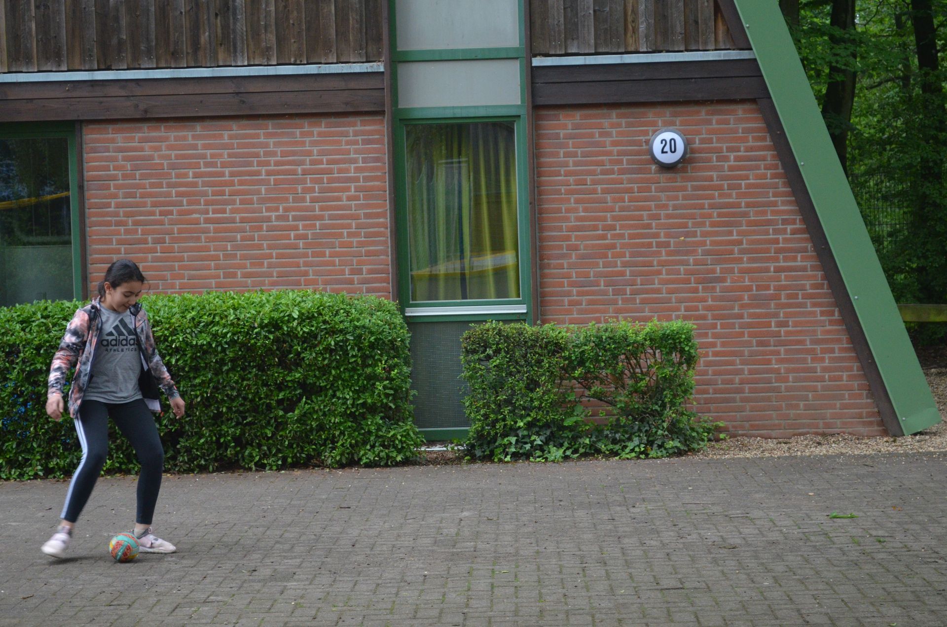 Ein Mädchen kickt vor einem Backsteingebäude Fußball  - Karate-Freizeit.