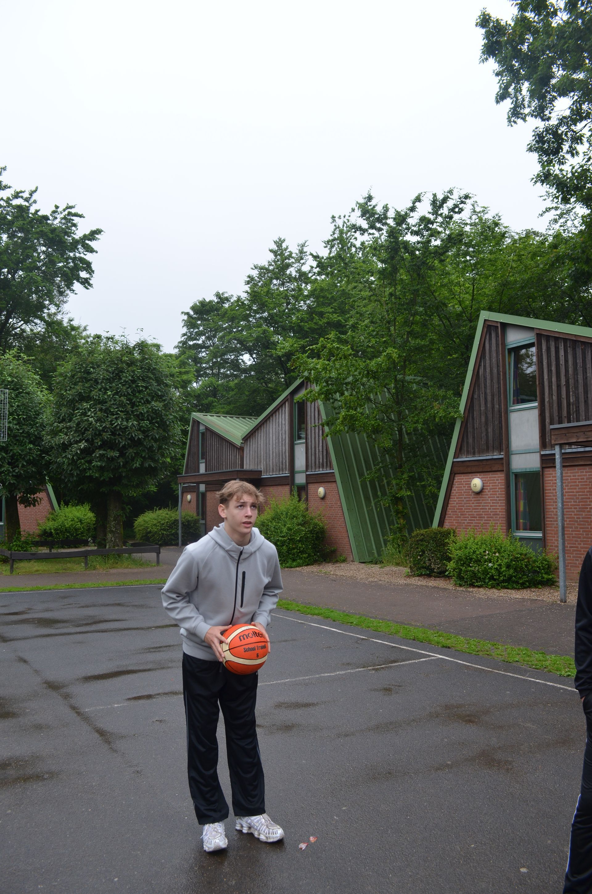 Ein Junge hält einen orangefarbenen Ball auf einem Parkplatz - Karate-Jugendfreizeit.