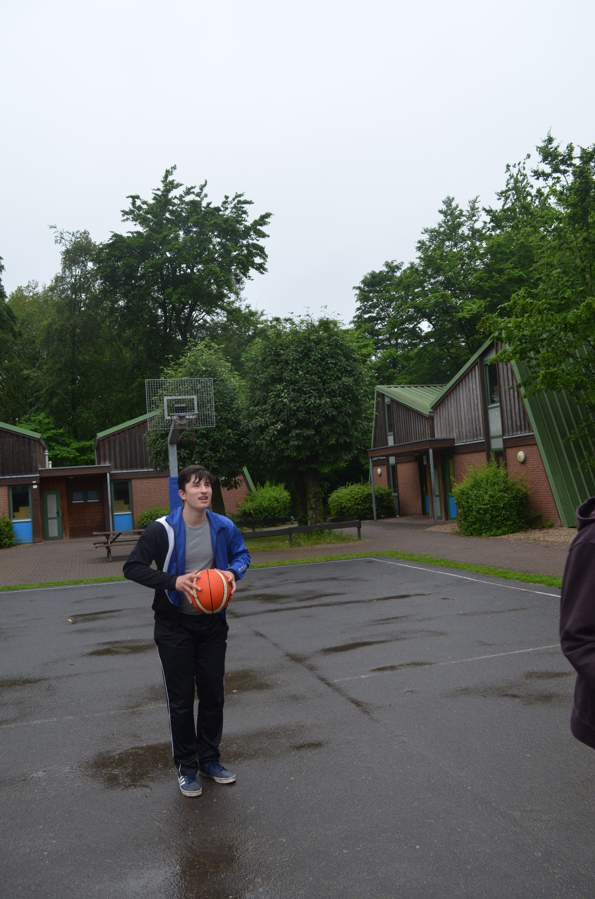 Ein Junge in einer blauen Jacke hält einen Basketball im Regen - Karate-Jugendfreizeit.