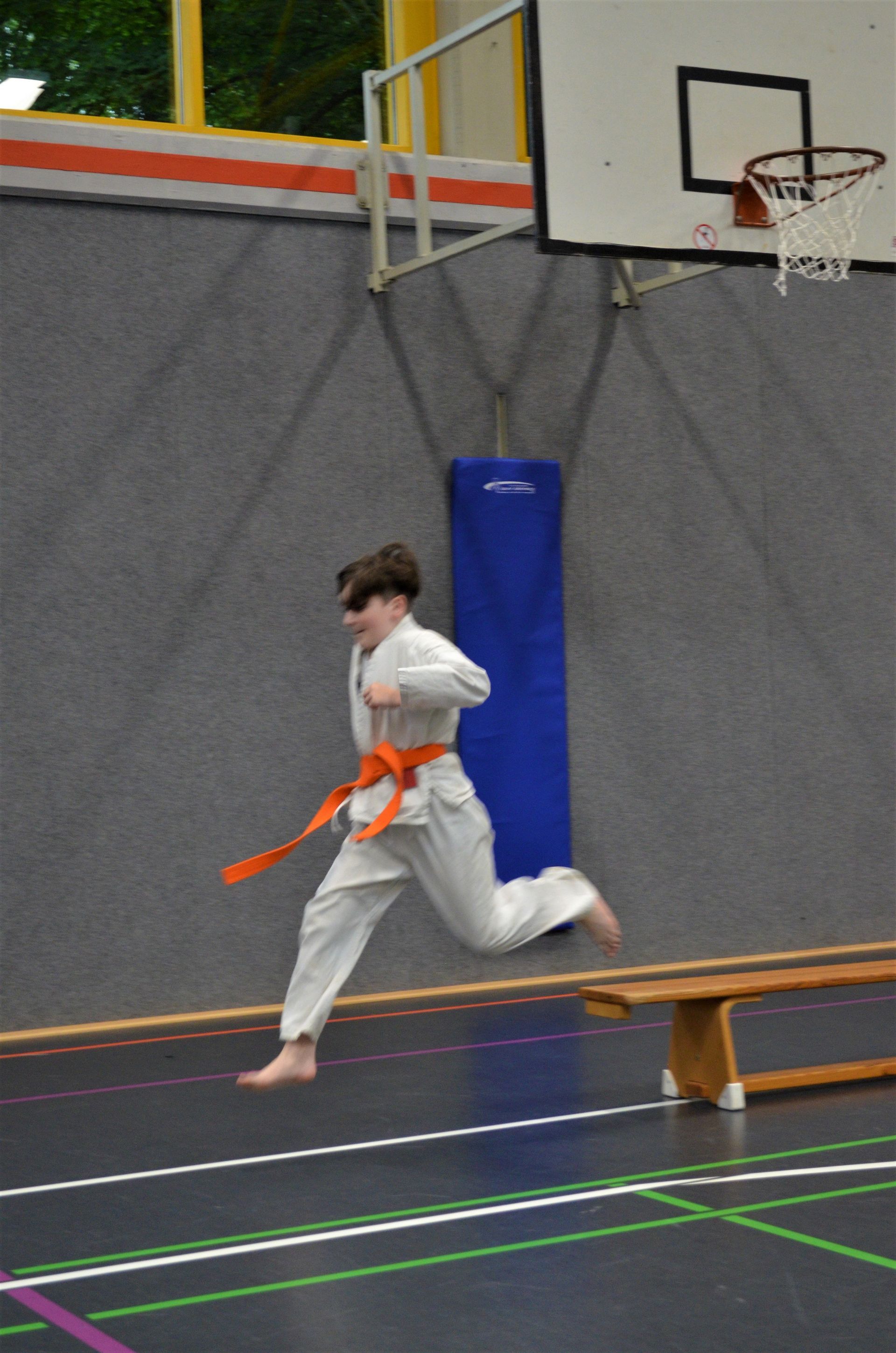 Ein kleiner Junge mit einem orangefarbenen Gürtel läuft in einem Fitnessstudio - Karate-Jugendfreizeit.
