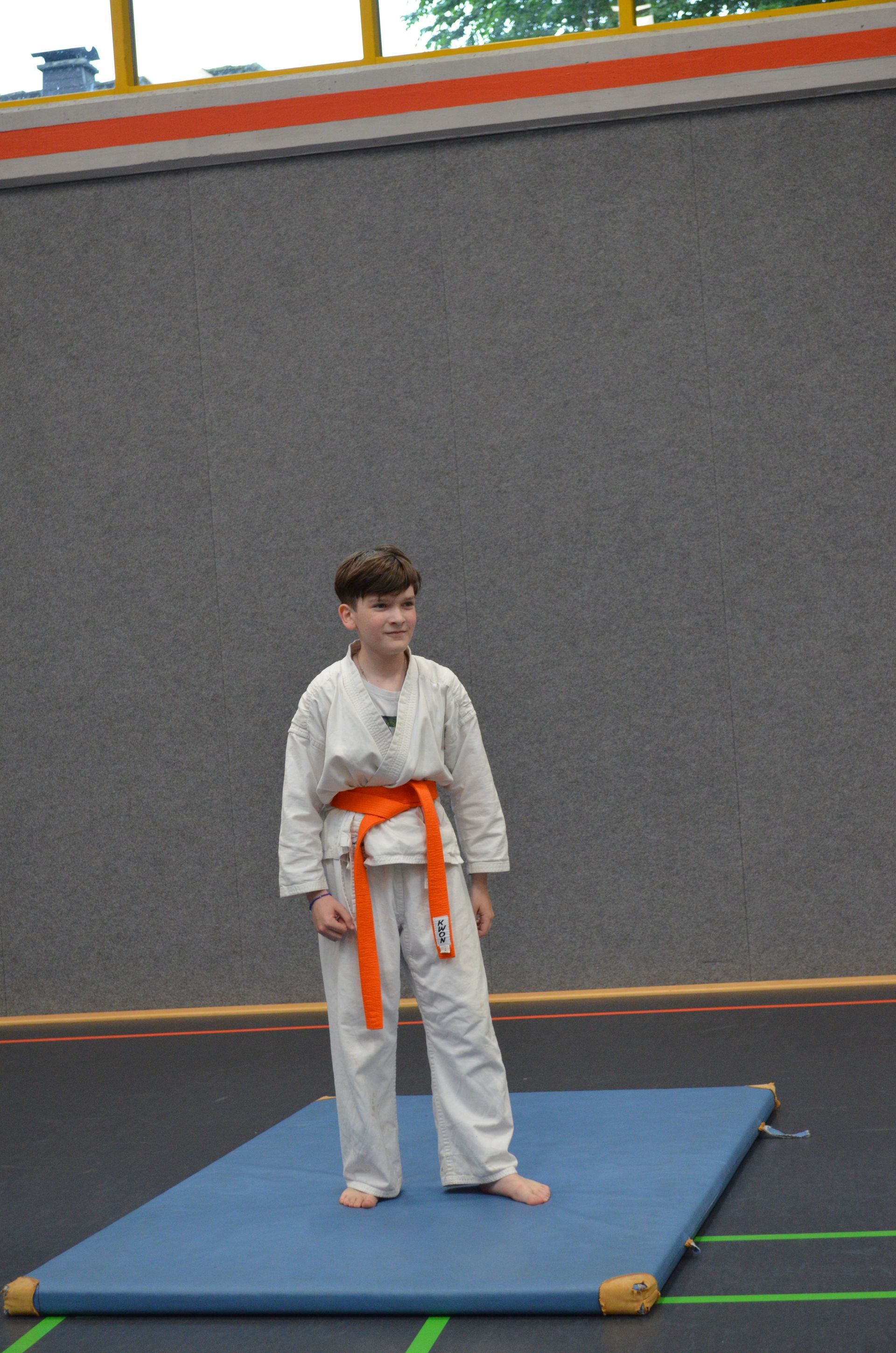 Ein kleiner Junge mit einem orangefarbenen Gürtel steht auf einer blauen Matte - Karate-Jugendfreizeit.