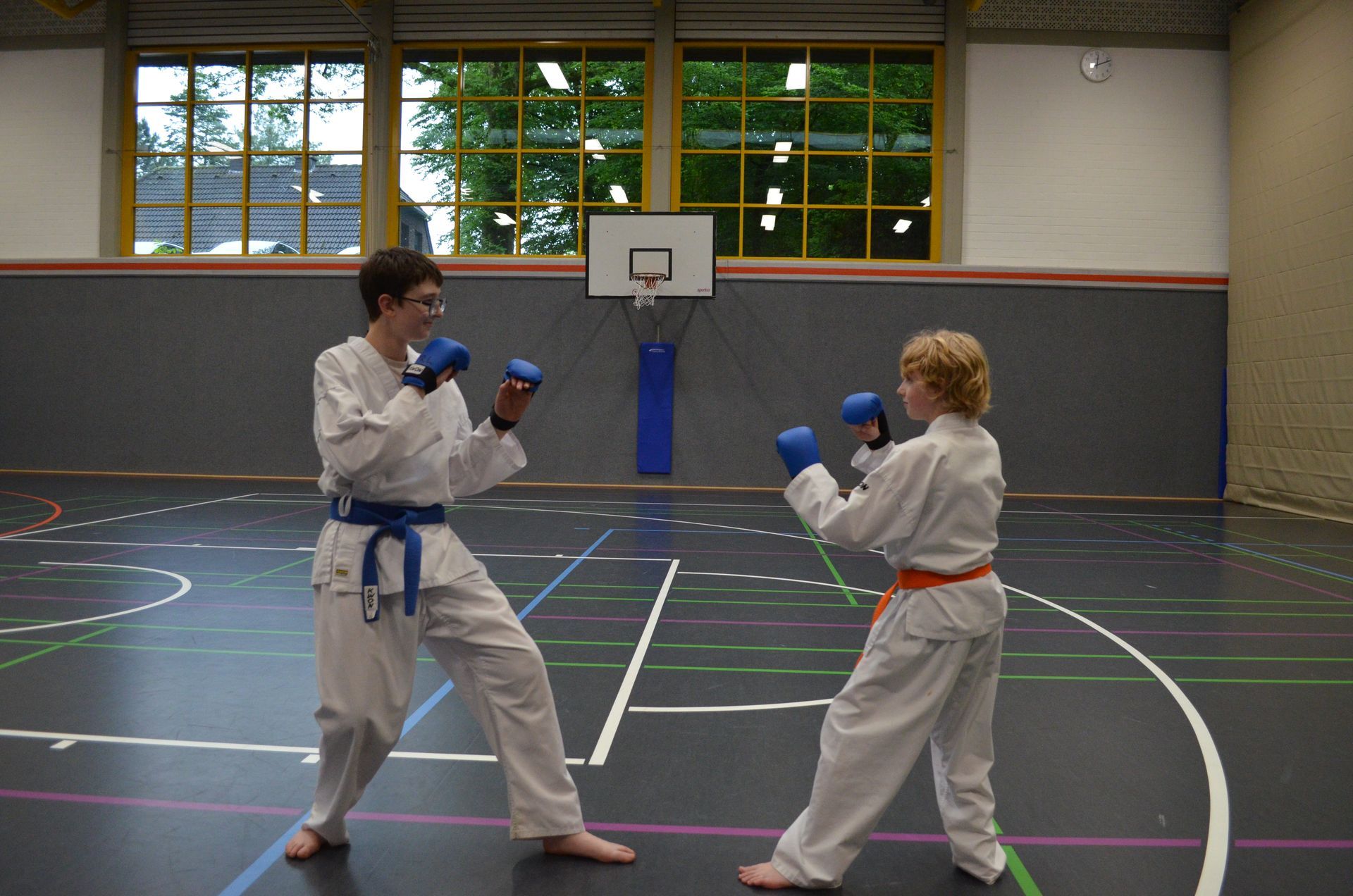 Zwei Personen boxen in einer Turnhalle mit einem Basketballkorb im Hintergrund - Karate-Jugendfreizeit.