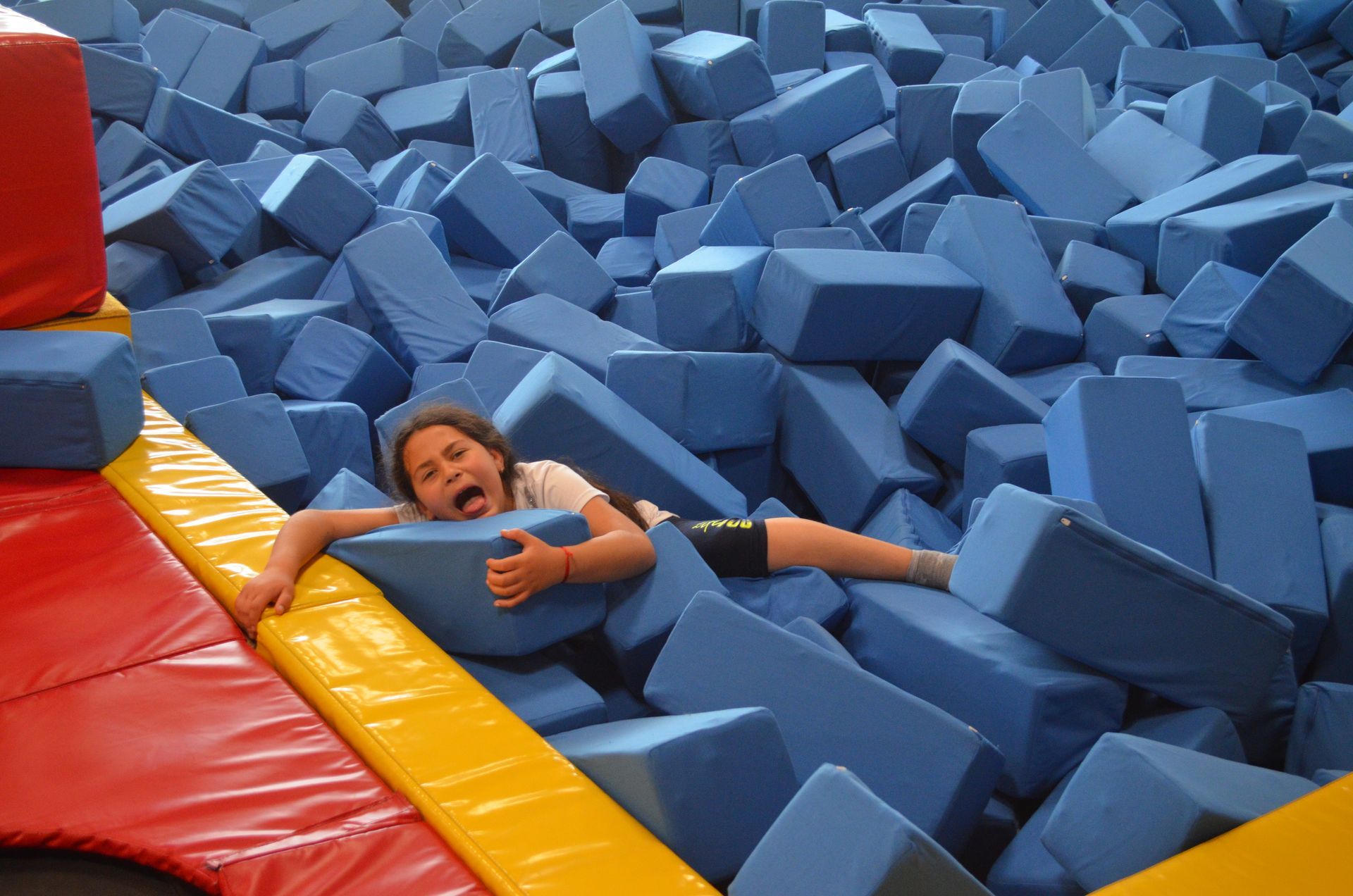 Ein Mädchen liegt in einem Stapel blauer Schaumstoffblöcke - Karate-Jugendfreizeit.