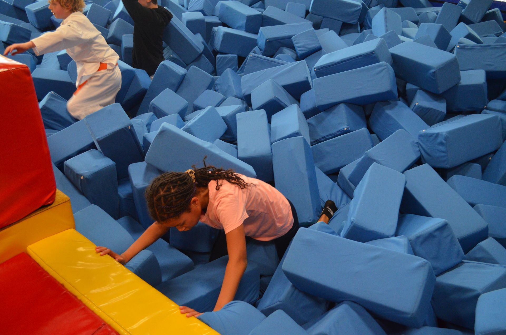 Ein Mädchen kriecht durch einen Stapel blauer Schaumstoffblöcke - Karate-Jugendfreizeit.