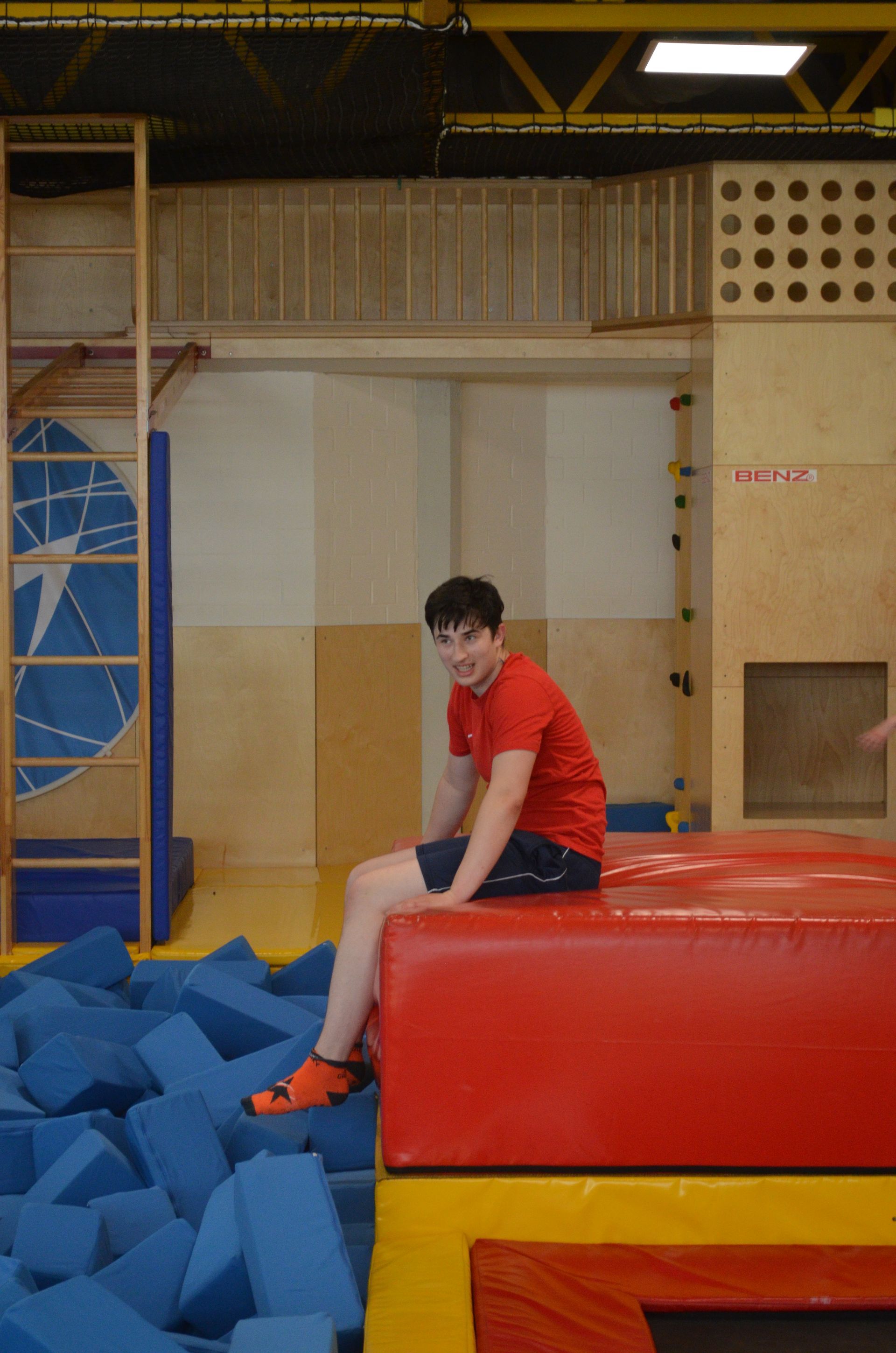 Ein Junge in einem roten Hemd sitzt in einer Turnhalle auf einem roten Block - Karate-Jugendfreizeit.