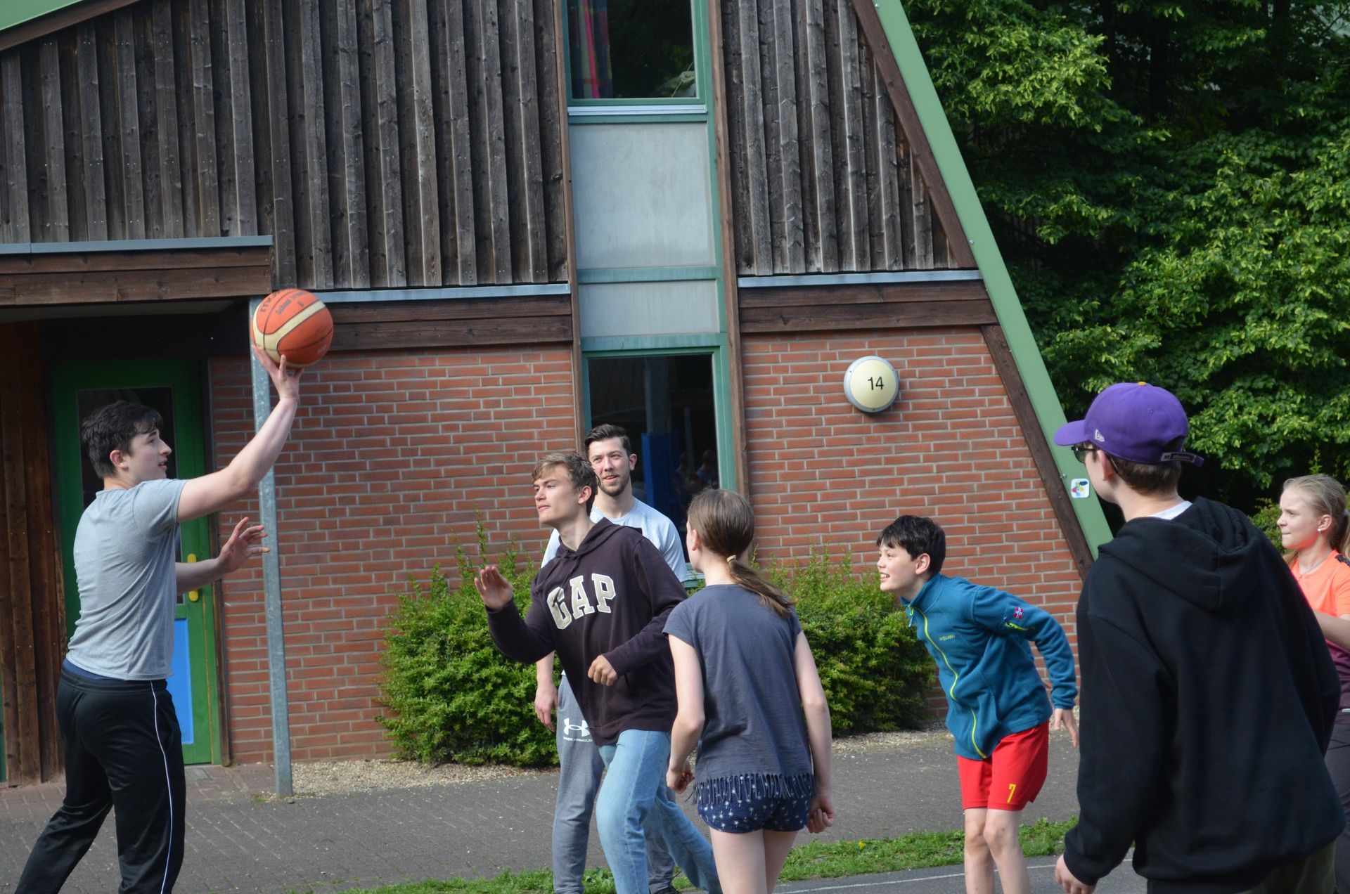 Eine Gruppe Kinder spielt Basketball vor einem Backsteingebäude - Karate-Jugendfreizeit.