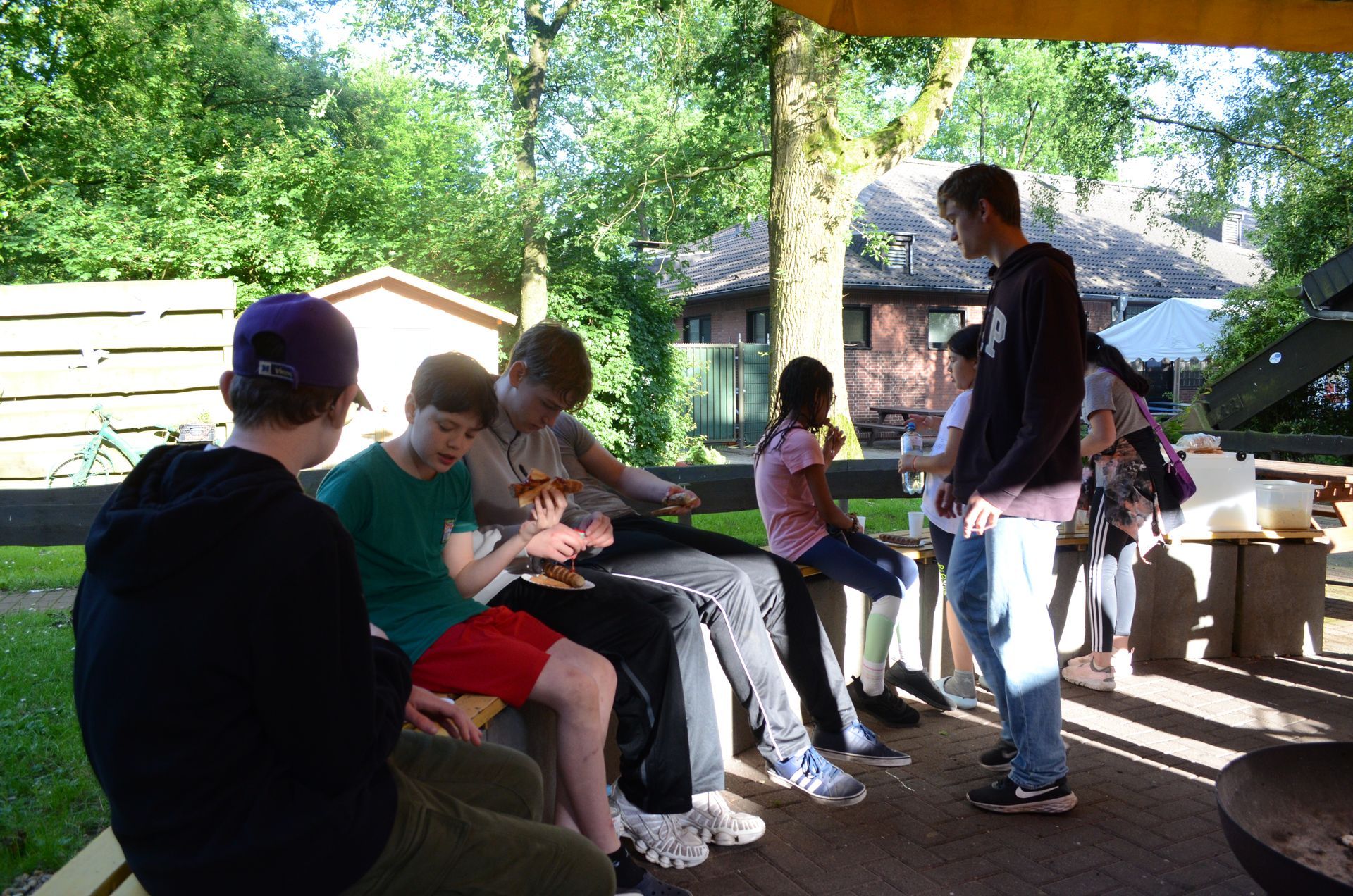 Eine Gruppe von Leuten sitzt auf einer Bank und isst Pizza - Karate-Jugendfreizeit.