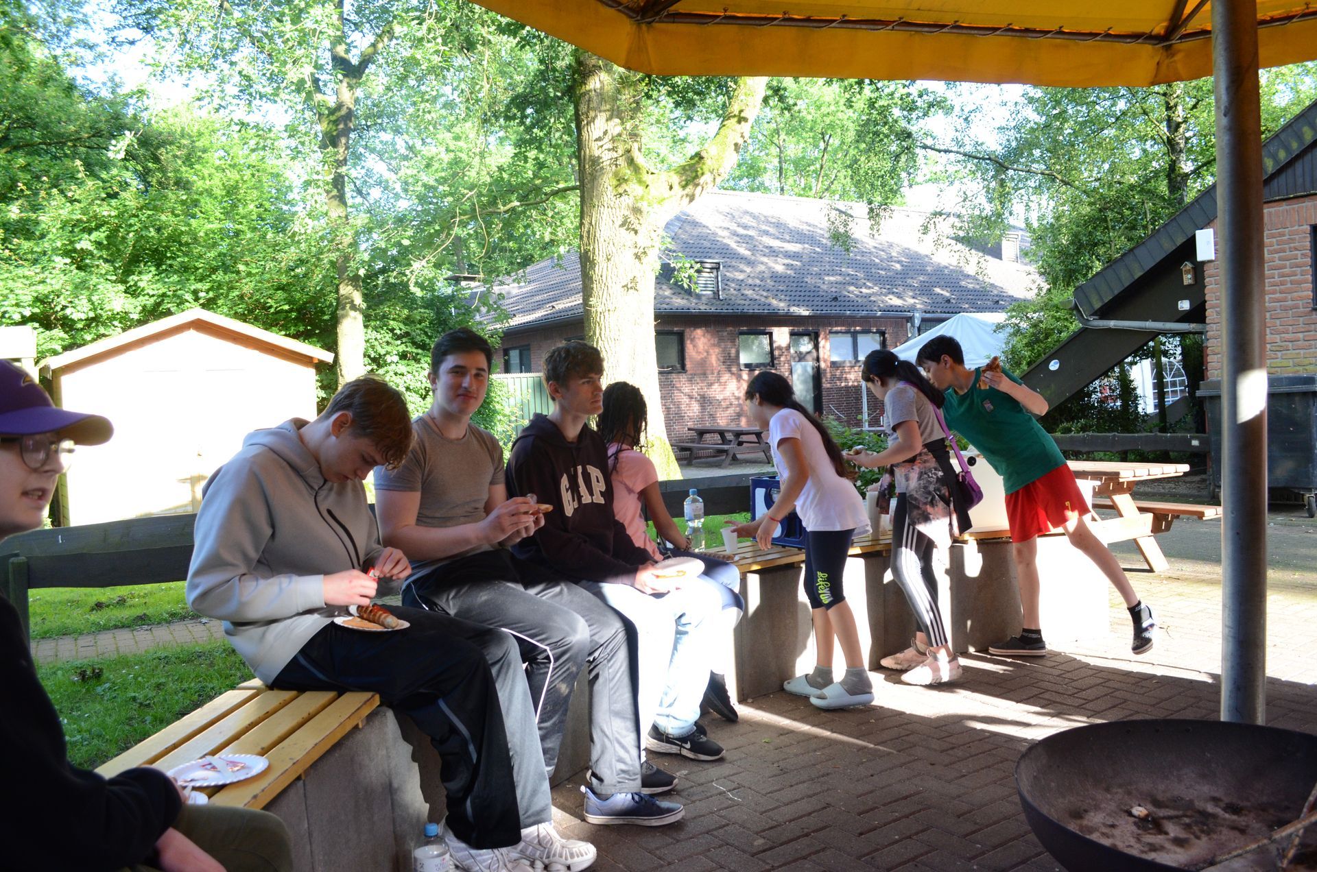 Eine Gruppe von Menschen sitzt auf Bänken unter einem Baldachin - Karate-Jugendfreizeit.