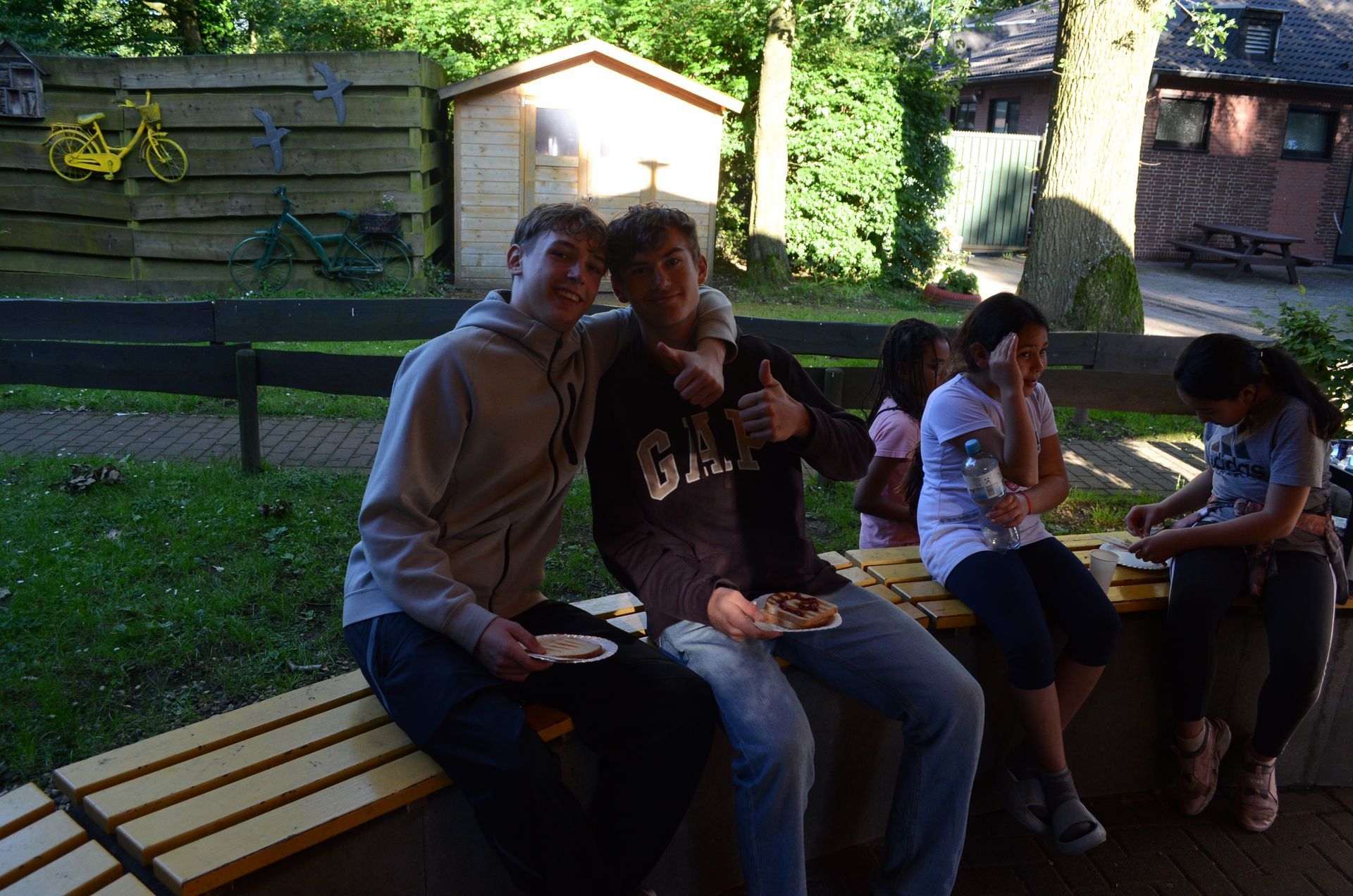 Eine Gruppe von Menschen sitzt auf einer Holzbank und isst Essen - Karate-Jugendfreizeit.