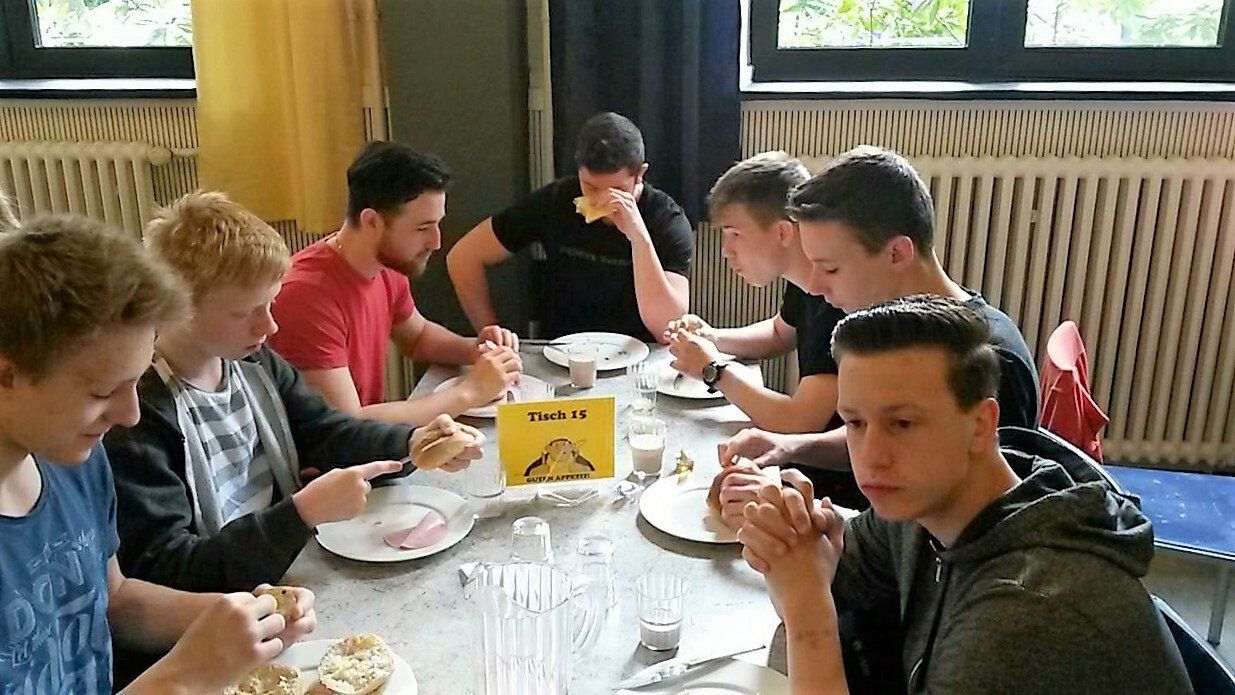 Eine Gruppe junger Männer sitzt an einem Tisch und isst.