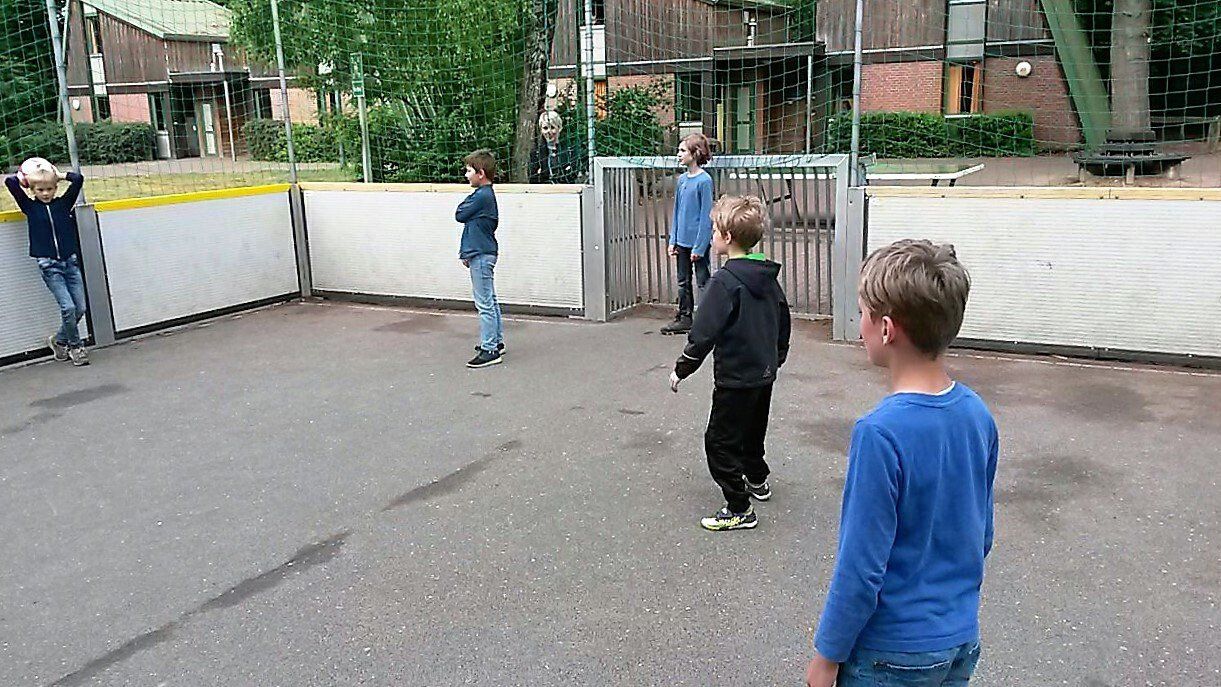 Eine Gruppe junger Jungen spielt in einem eingezäunten Bereich Fußball.