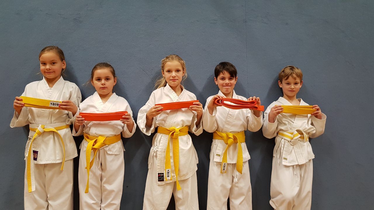 Eine Gruppe von Kindern in Karateuniformen steht nebeneinander und hält Gürtel.