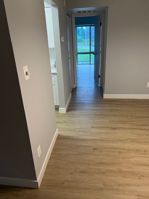 Hallway with wood-look flooring, gray walls, and an open door leading outside.