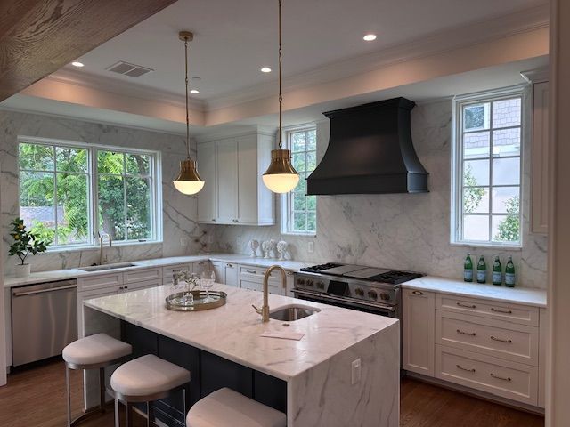 A kitchen with white cabinets , a large island , a stove , a sink , and a hood.