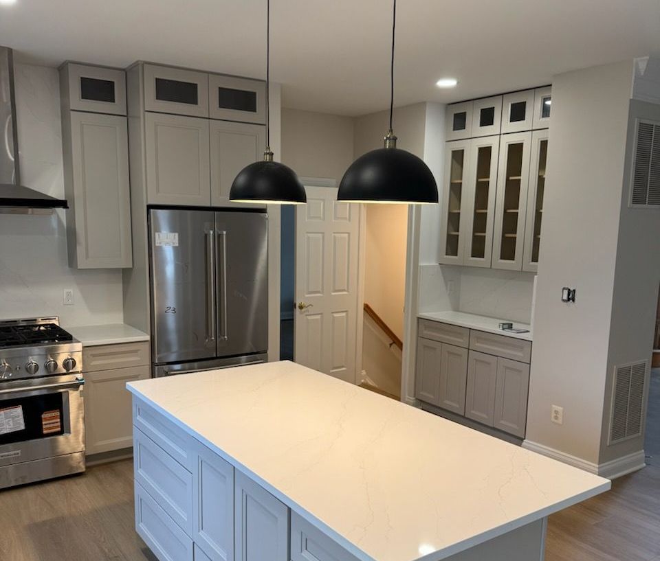 Modern kitchen with gray cabinets, stainless steel appliances, white island, and black pendant lights.