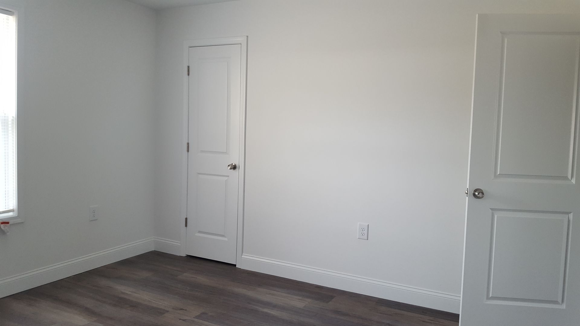 An empty bedroom with hardwood floors and white walls.