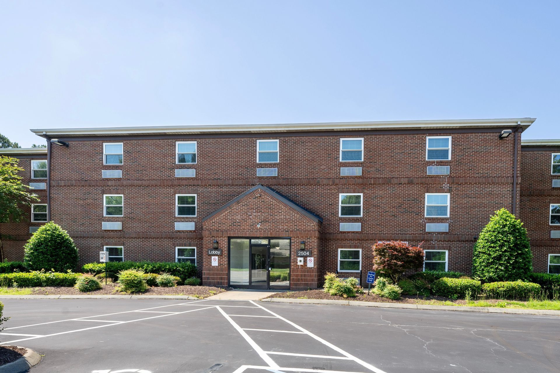 A large brick building with a lot of windows and a parking lot in front of it.