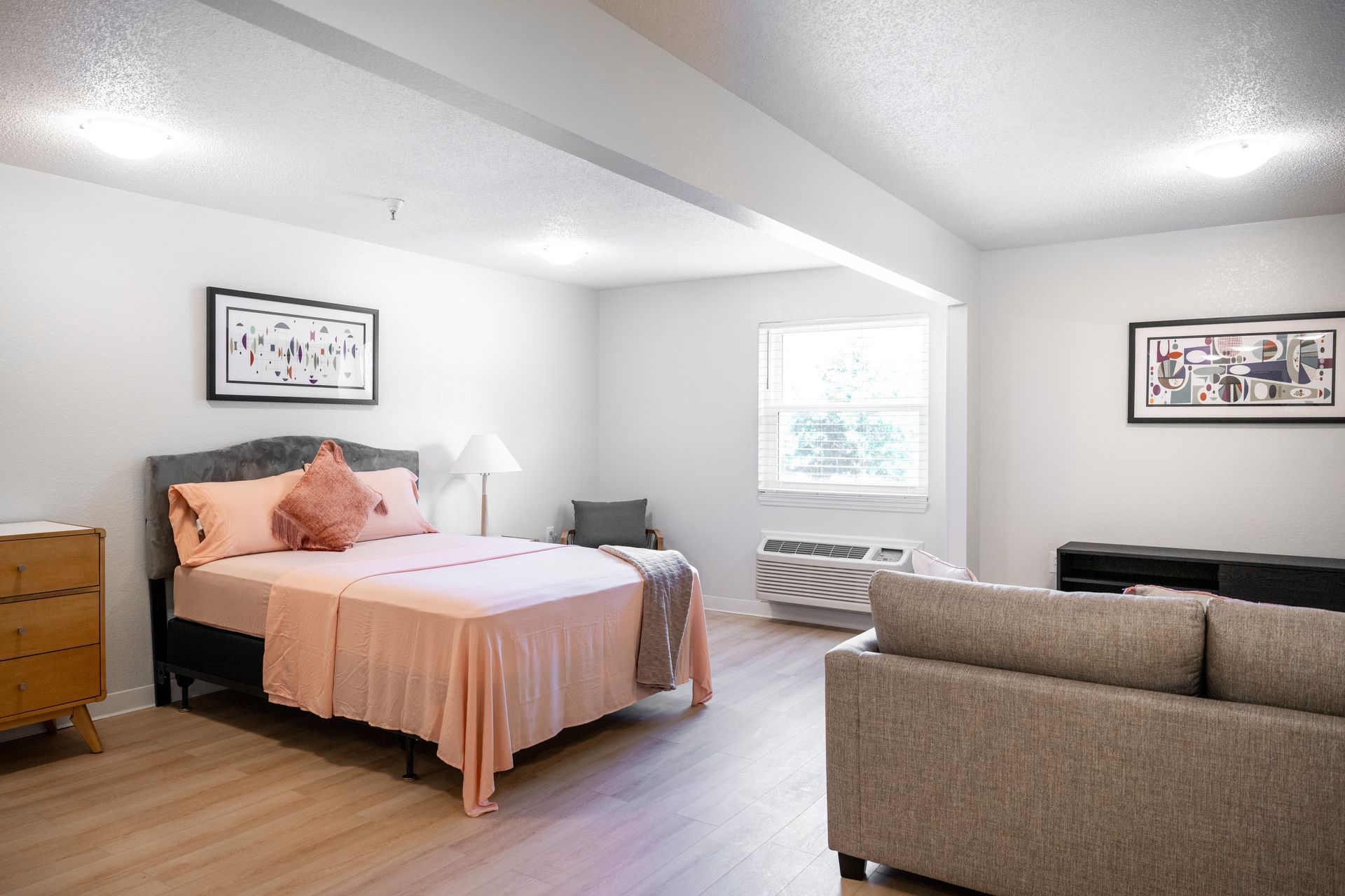 A bedroom with a bed , couch , nightstand and window.