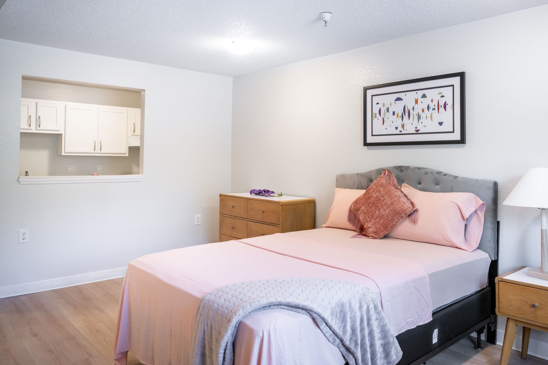 A bedroom with a bed , nightstand , lamp and dresser.
