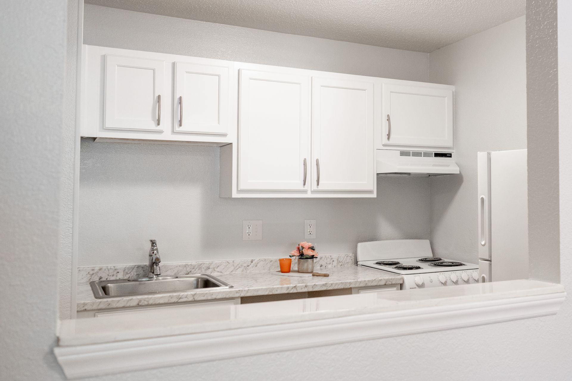 A kitchen with white cabinets , a sink , stove and refrigerator.
