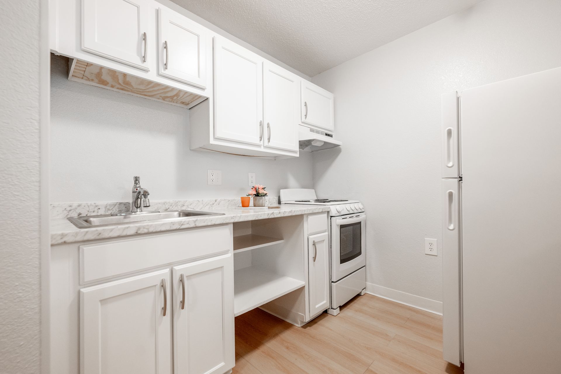 A kitchen with white cabinets , a stove , a refrigerator , and a sink.